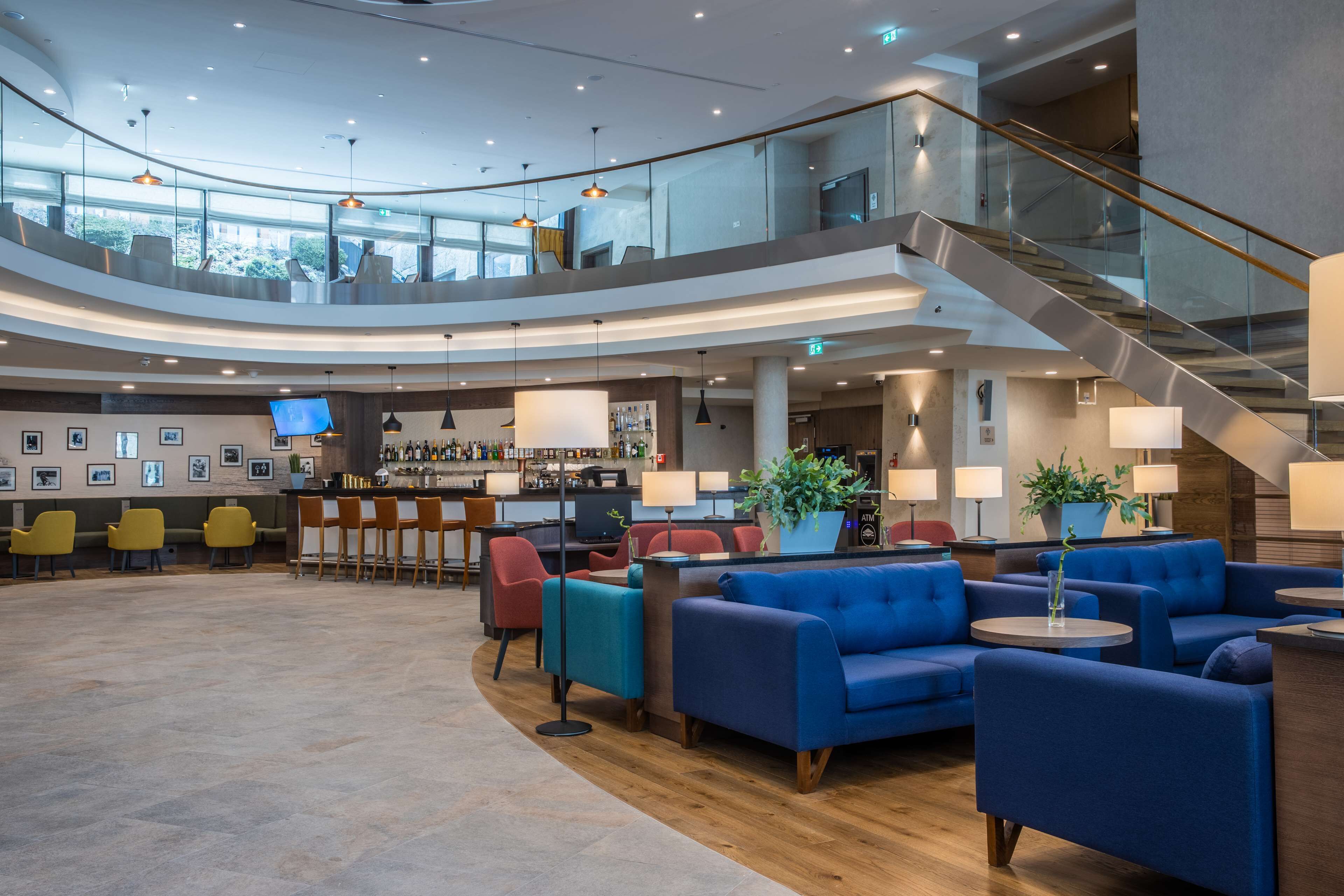 Un lobby amplio con una escalera curva, zonas de estar, un bar y una planta grande.