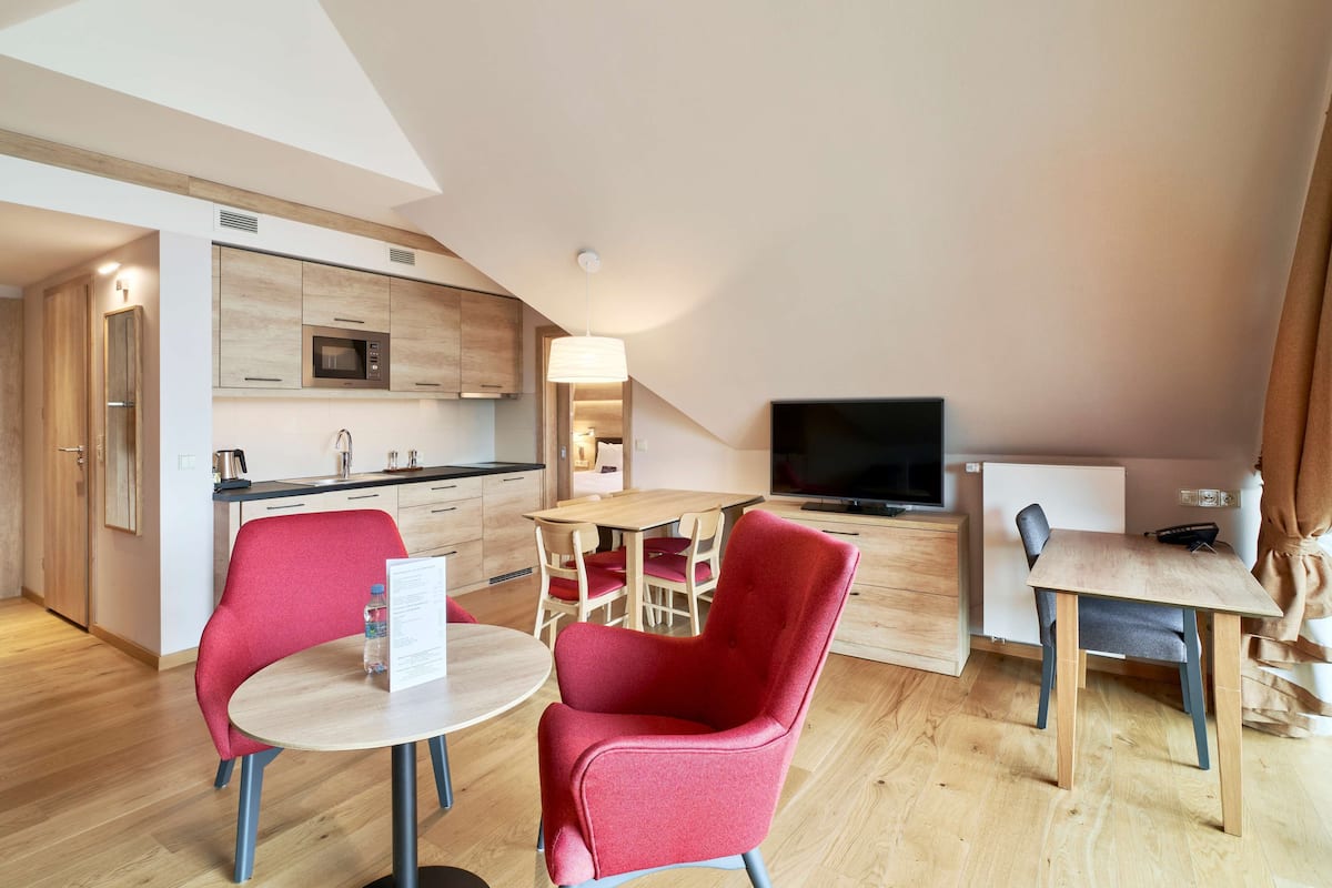 Cocina moderna con armarios de madera, microondas y comedor con sillas rojas y una mesa.