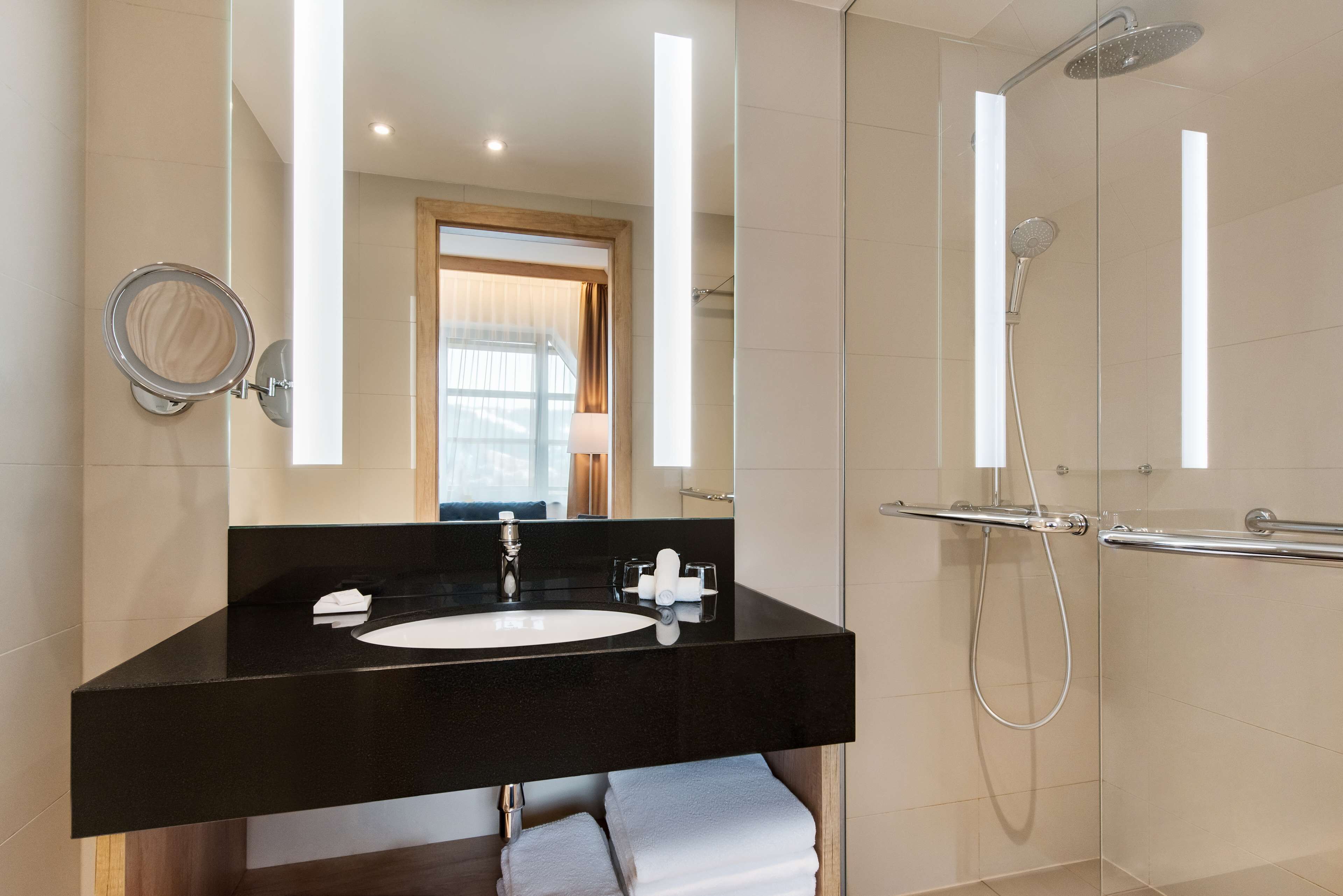 Un baño moderno con lavamanos de superficie negra, un espejo y cabina de ducha con paredes de vidrio.