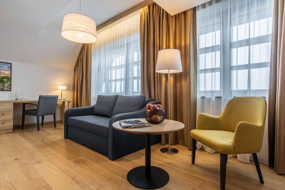 Habitación de hotel moderna con sofá, sillón y mesa redonda con frutero.