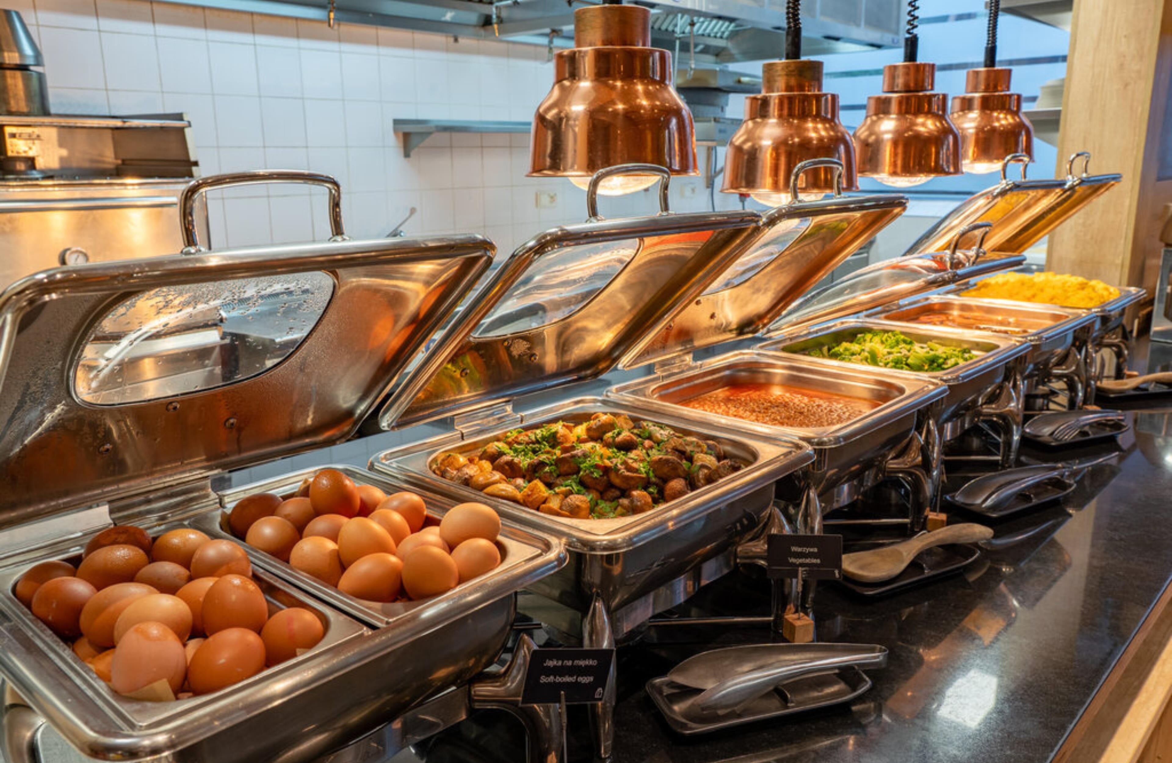 A buffet with various food options, including eggs, vegetables, and other dishes, in a well-lit kitchen area with copper lighting fixtures.
