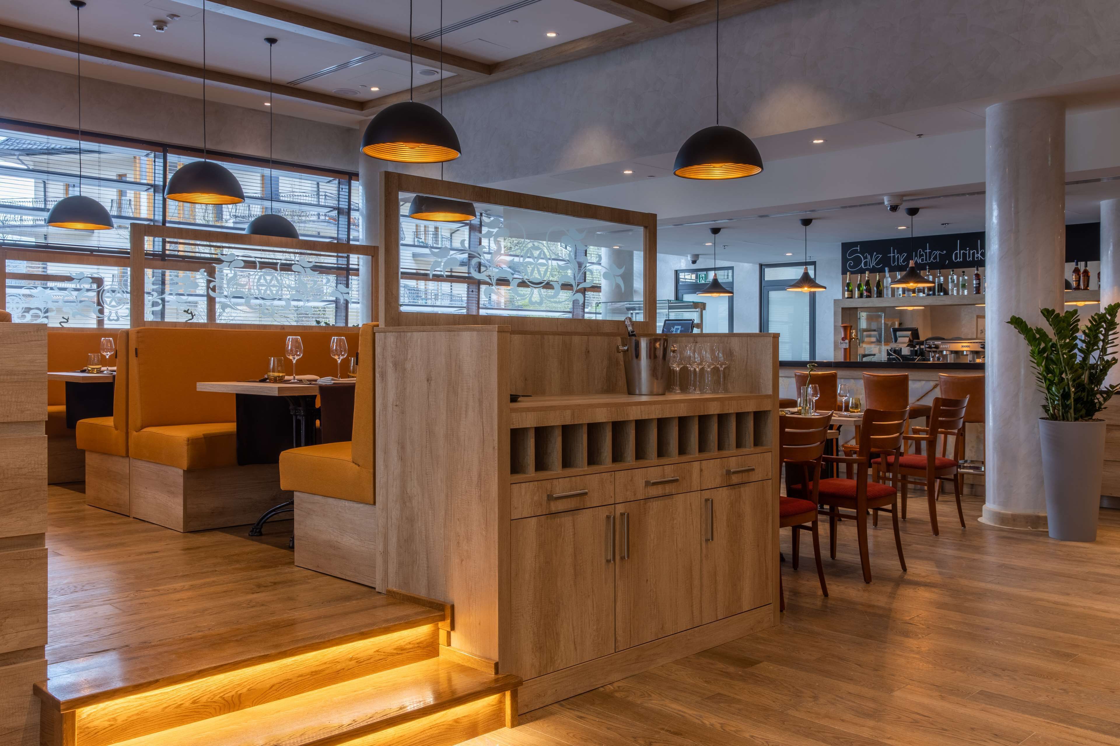 Interior de un restaurante moderno con mobiliario de madera, iluminación colgante y una zona de bar.