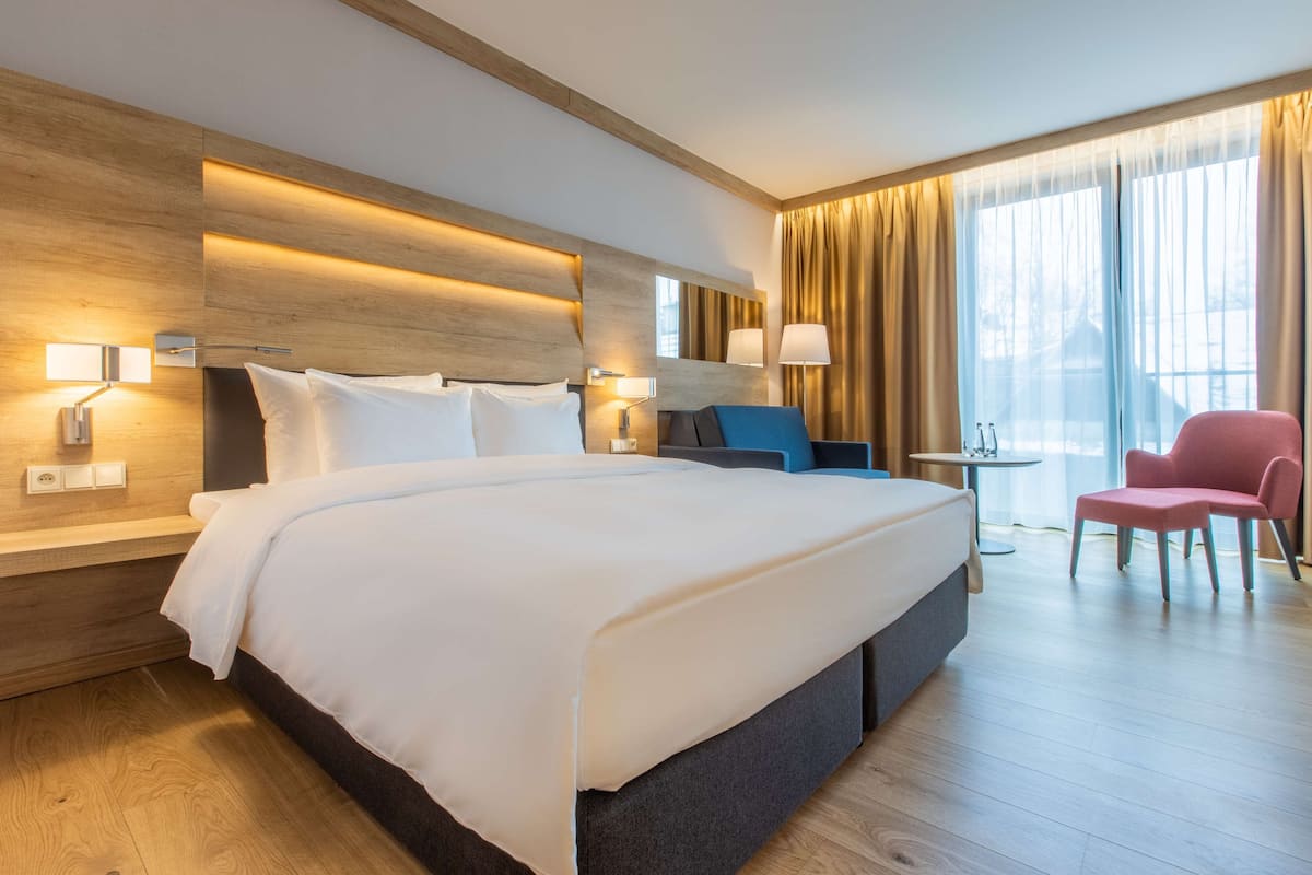 Una habitación de hotel moderna con una cama grande, mesitas de noche, un escritorio, una silla y un ventanal con cortinas.
