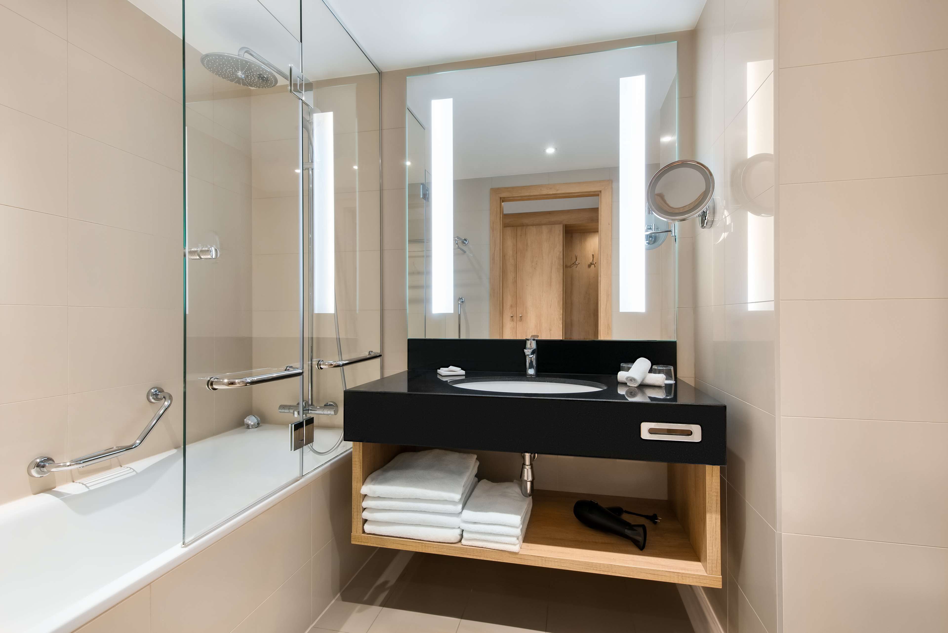 A modern bathroom with a glass-enclosed shower, a black sink vanity, and a wooden shelf with towels.