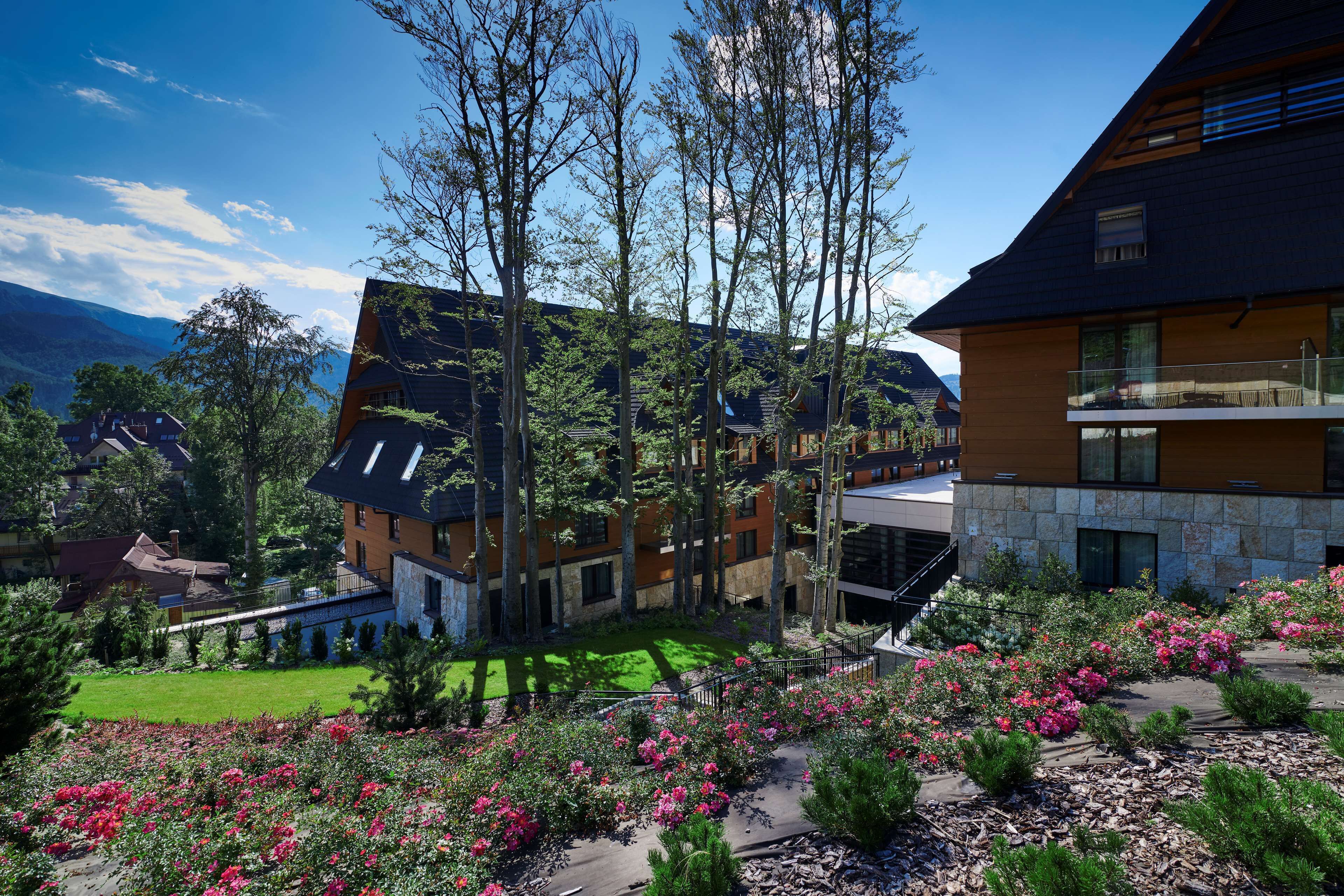 A modern building with a stone facade and a balcony overlooking a landscaped garden with pink flowers.