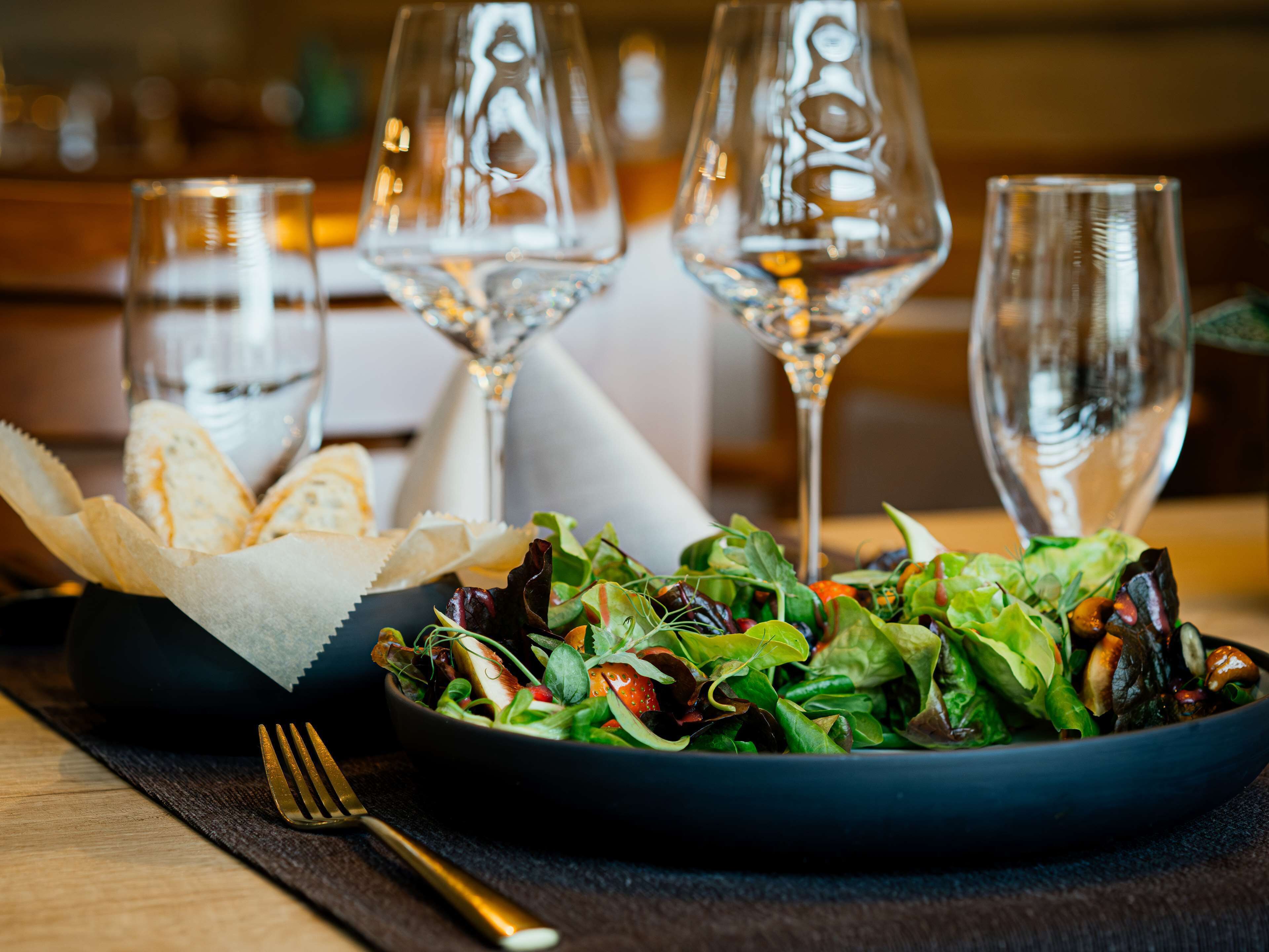 Een saladekom met een vork en een servet ernaast, en drie wijnglazen op de achtergrond.