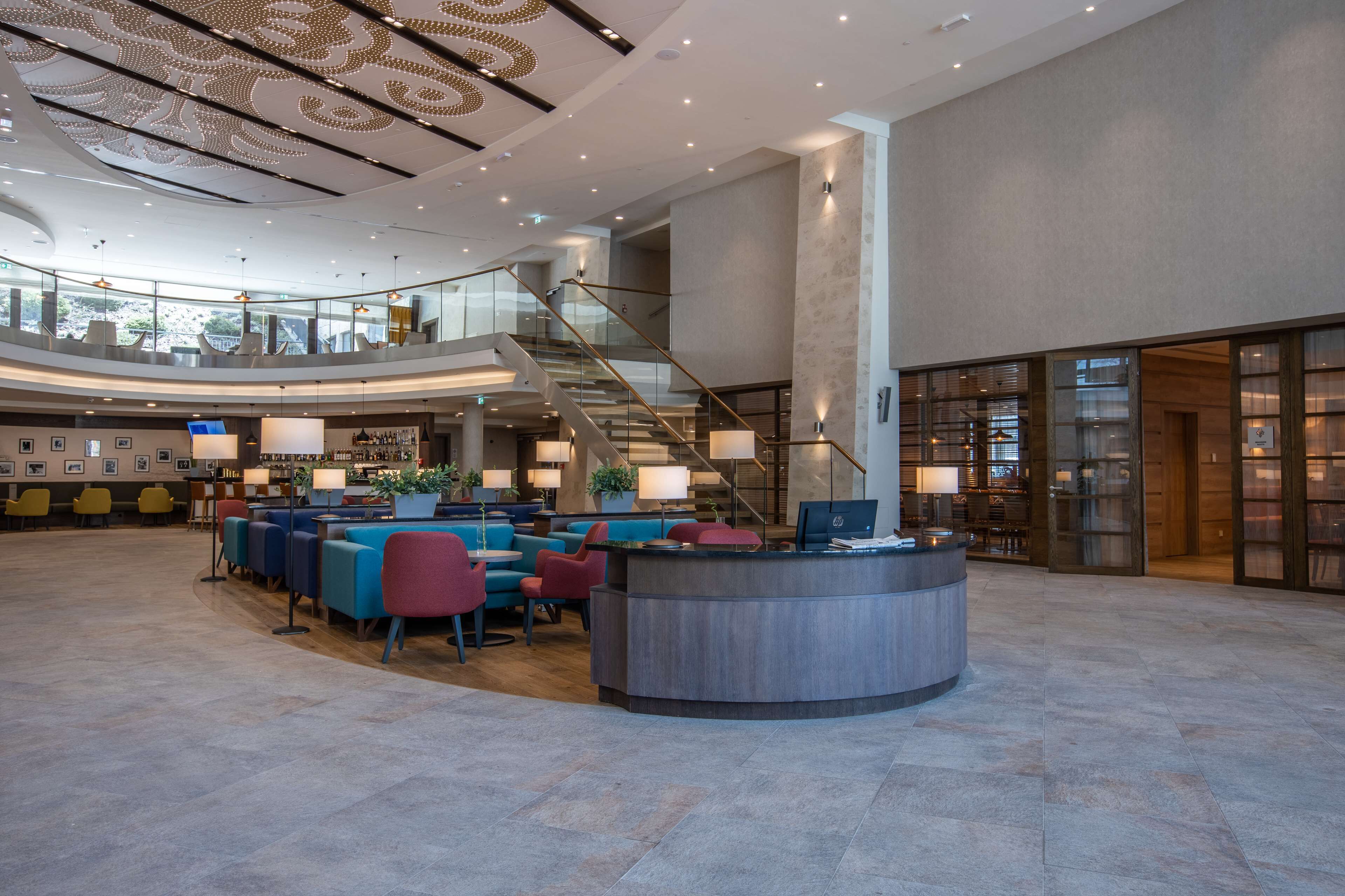 A spacious lobby with a curved reception desk, seating area, and a staircase leading to upper floors.