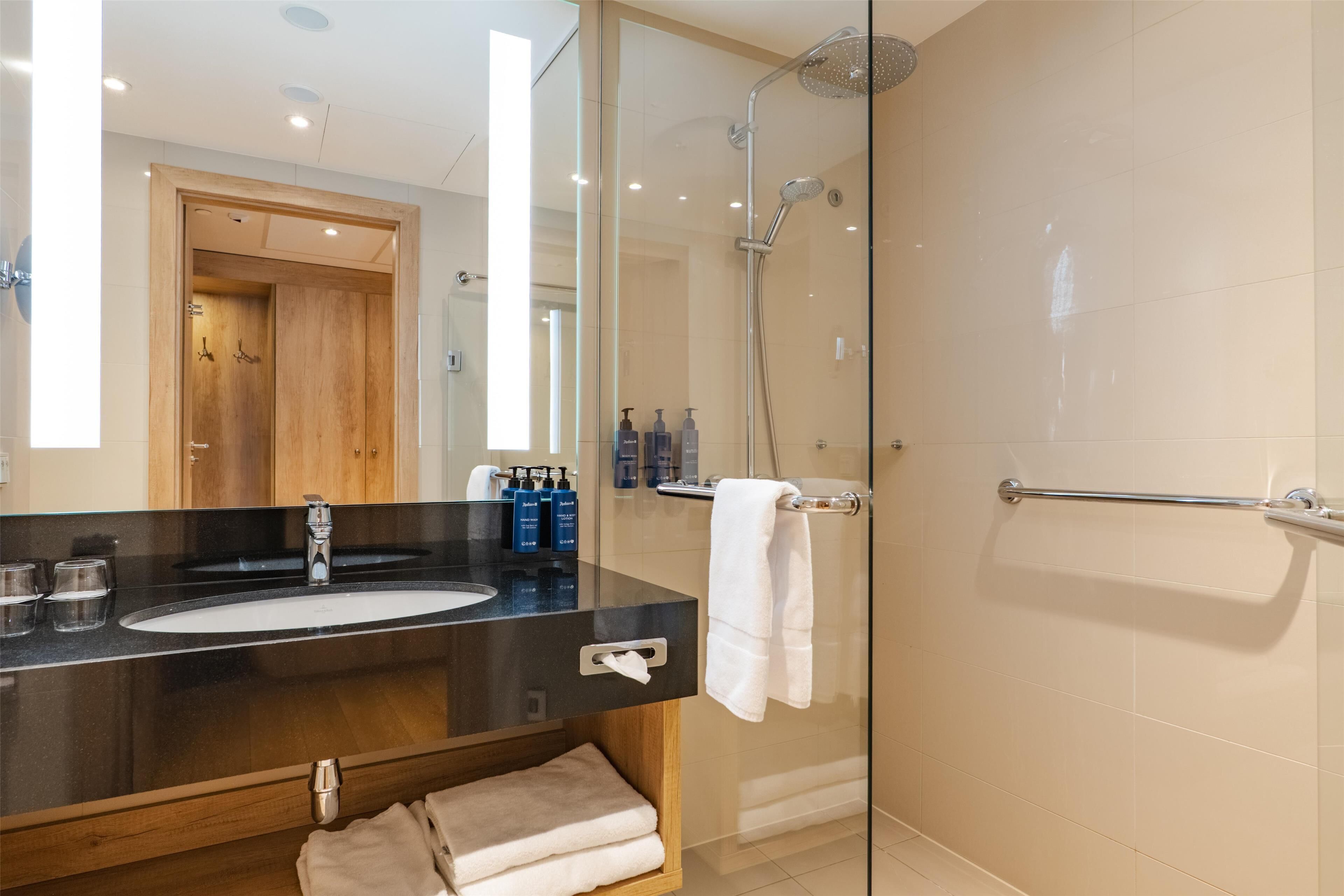 Une salle de bain moderne avec une douche à parois de verre, un lavabo sur un plan de toilette noir et un meuble-lavabo en bois.