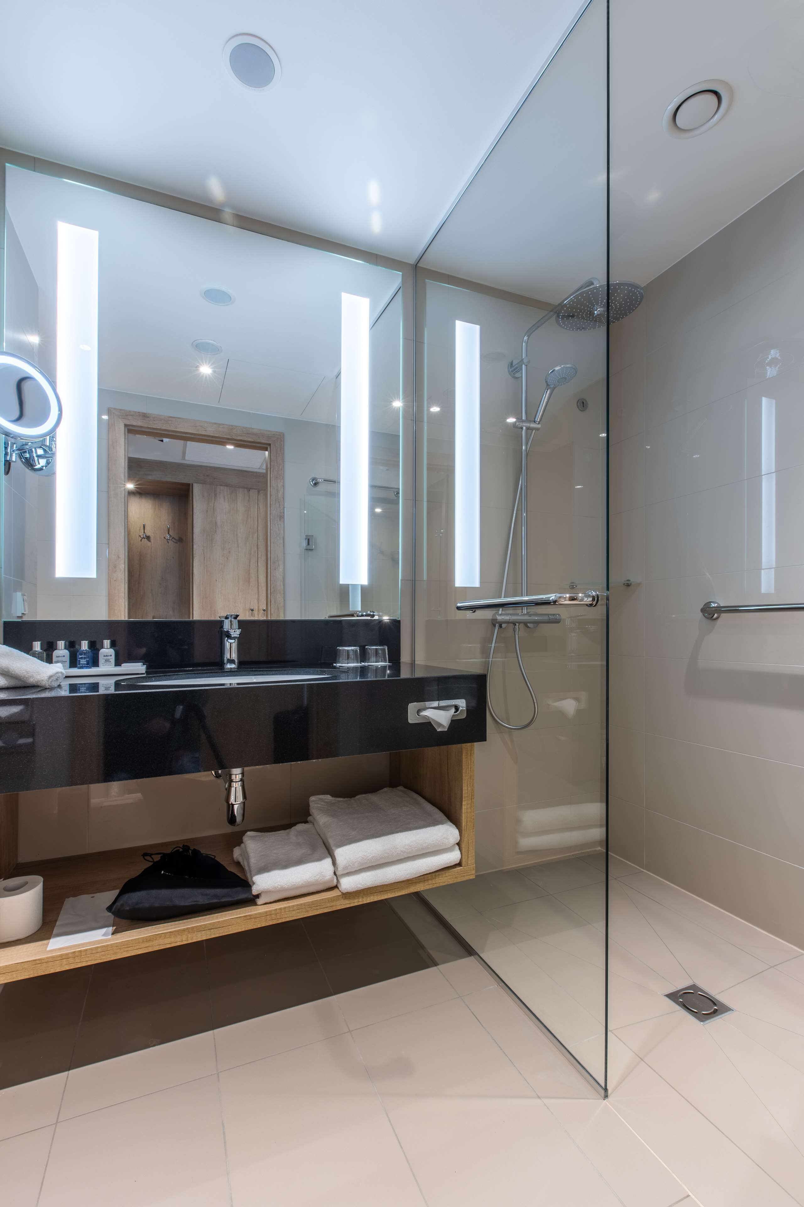 Une salle de bain moderne dotée d’une douche à parois de verre, d’un grand miroir et d’un meuble-lavabo avec un plan de travail noir.