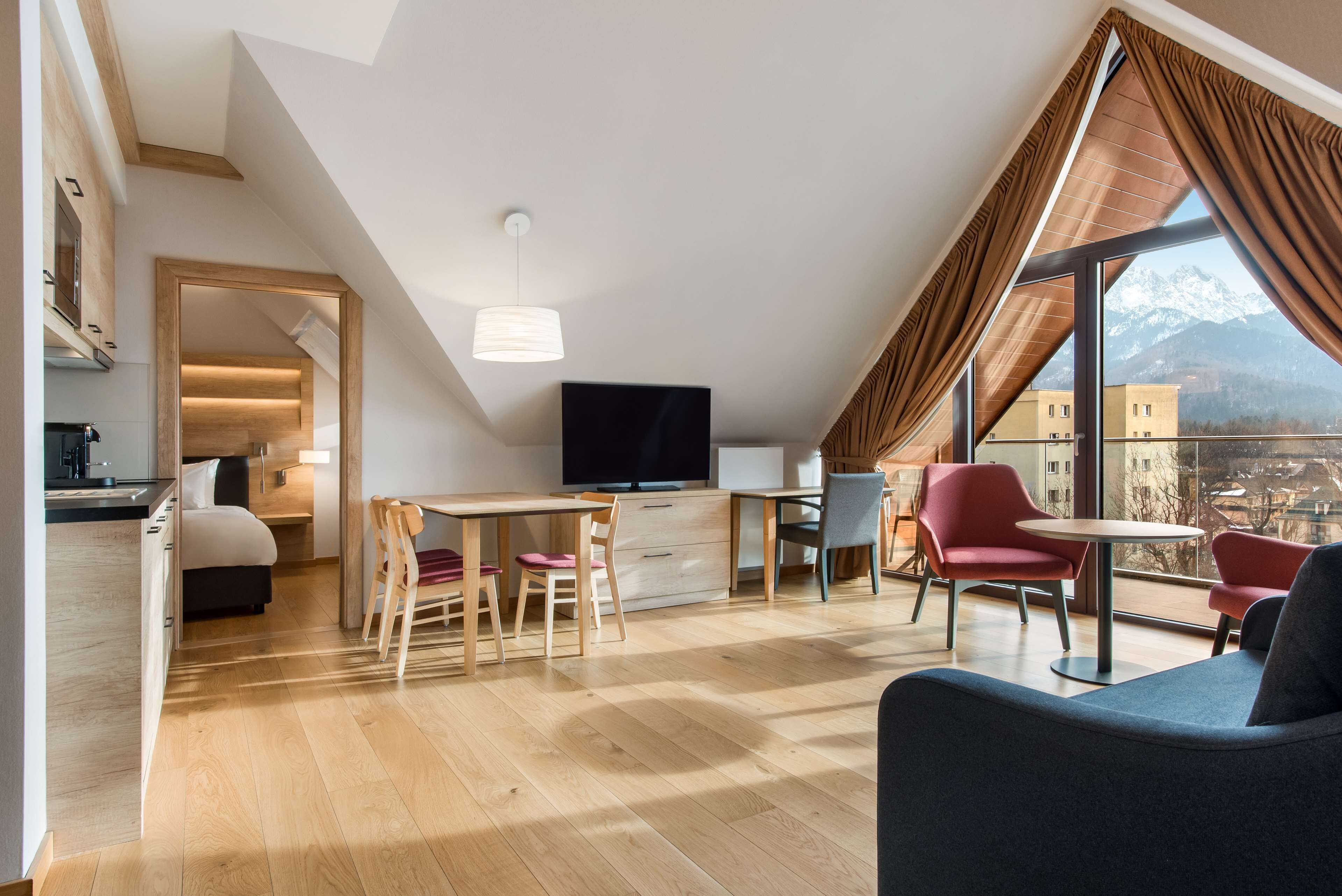 Un dormitorio tipo loft moderno con un ventanal grande, un televisor de pantalla plana y una zona de comedor con sillas rojas.