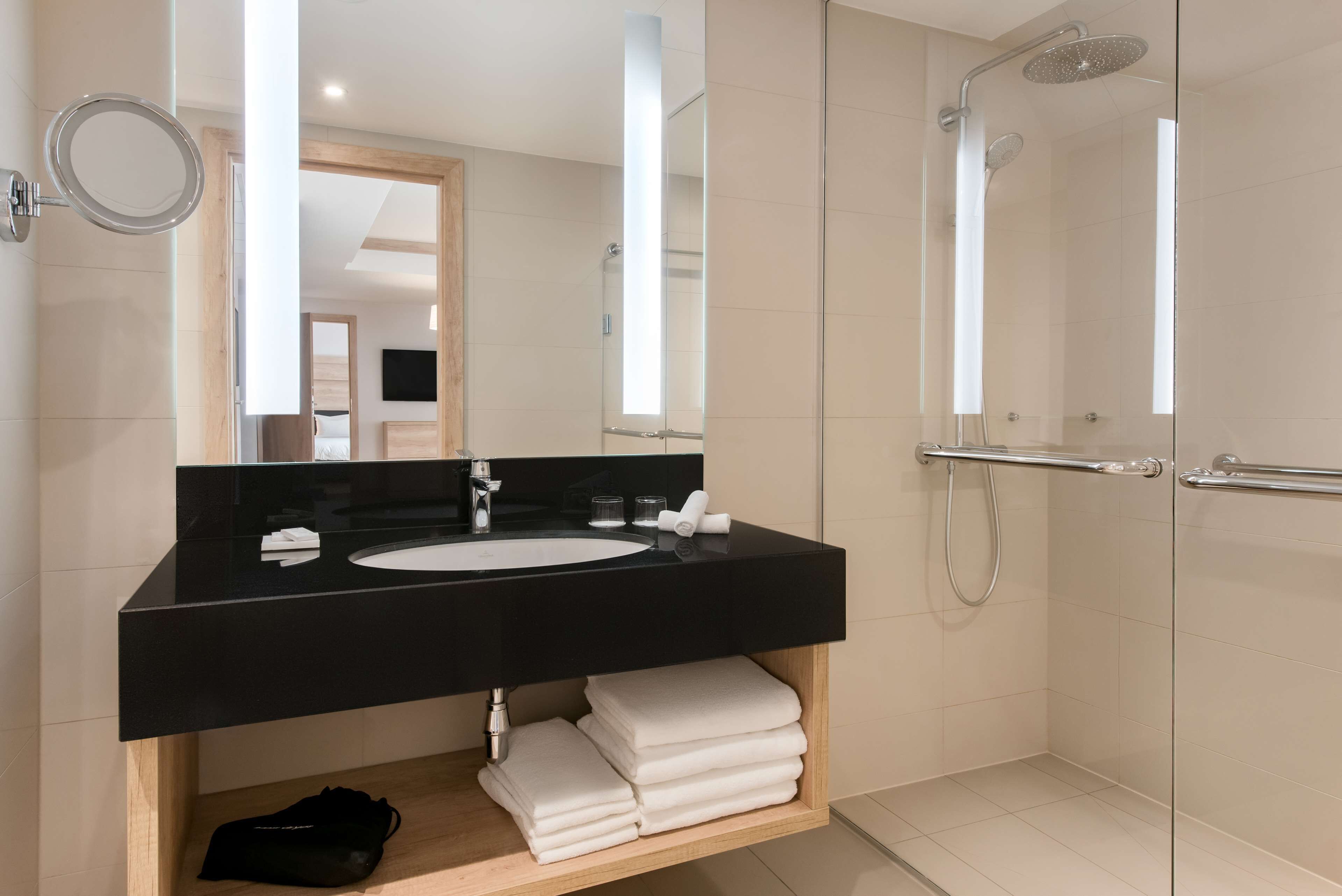 Ein modernes Badezimmer mit einem schwarzen Waschbecken, einem Spiegel, einer Duschkabine und ordentlich gefalteten weißen Handtüchern.