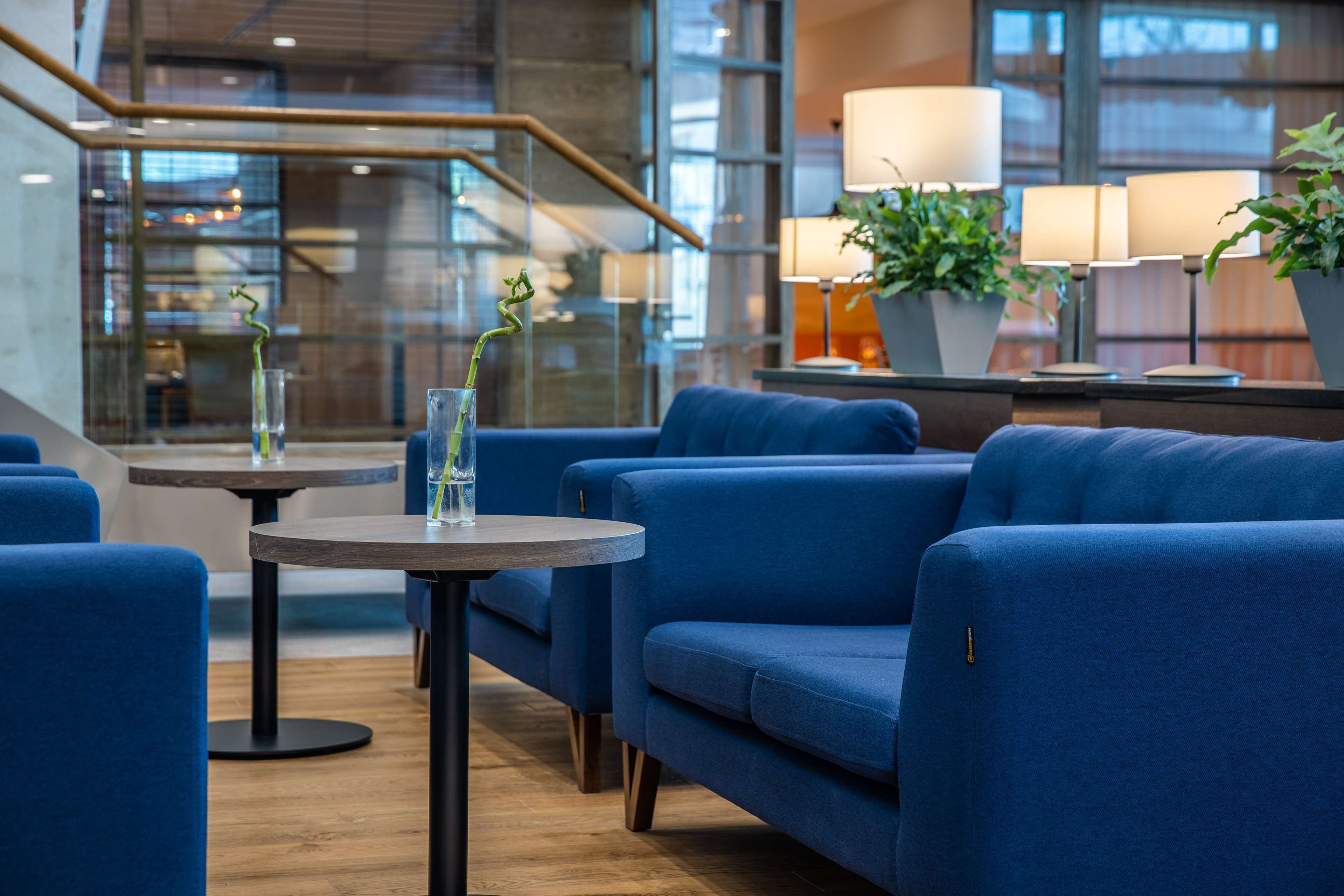 A modern lounge area with blue sofas, a round table, and potted plants.
