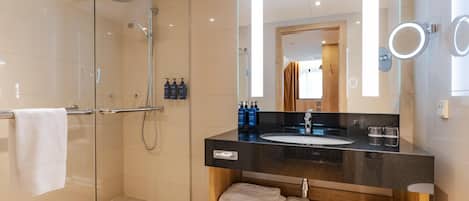 A modern bathroom with a glass-enclosed shower, a black countertop sink, wooden vanity, and a large mirror with integrated lighting.