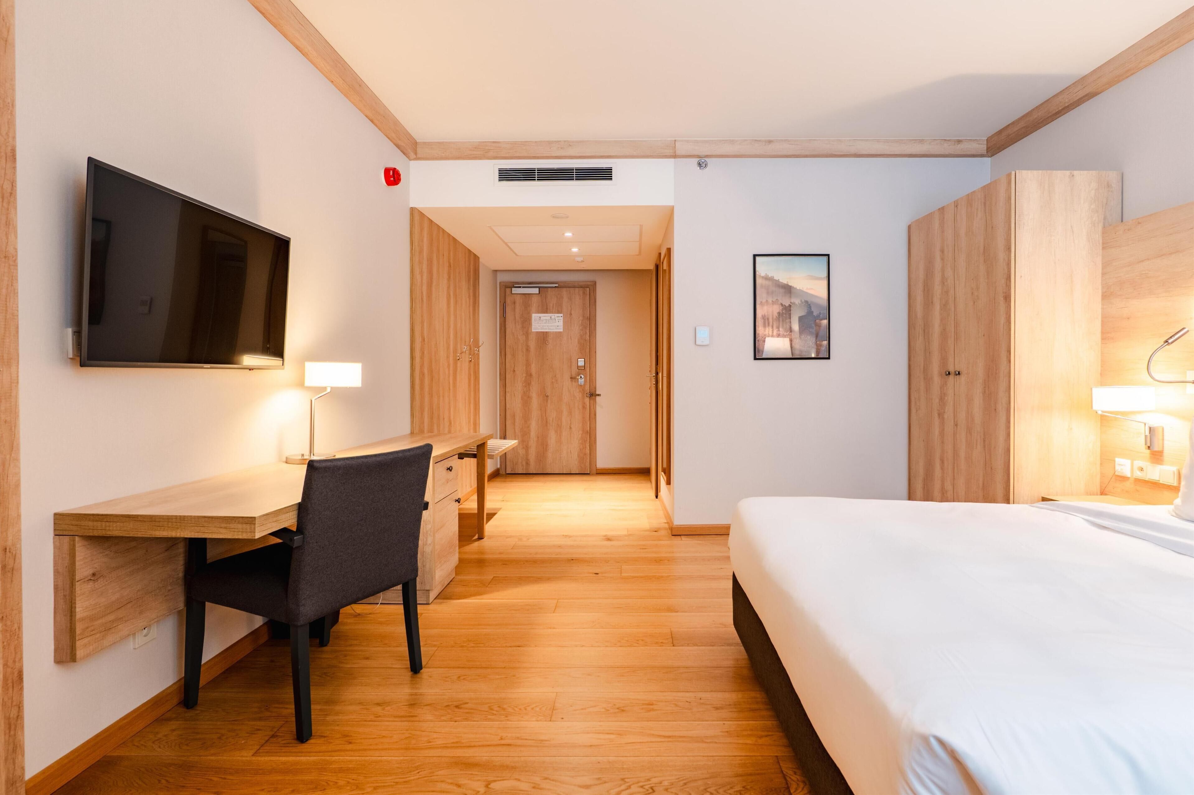 Habitación de hotel con cama, escritorio, silla, televisor y puerta que da a otra habitación.