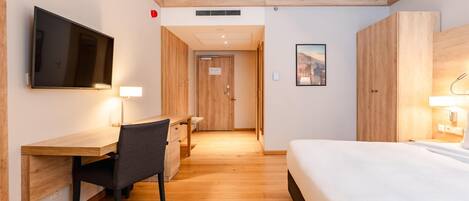 Habitación de hotel con cama, escritorio, silla, televisor y puerta que da a otra habitación.