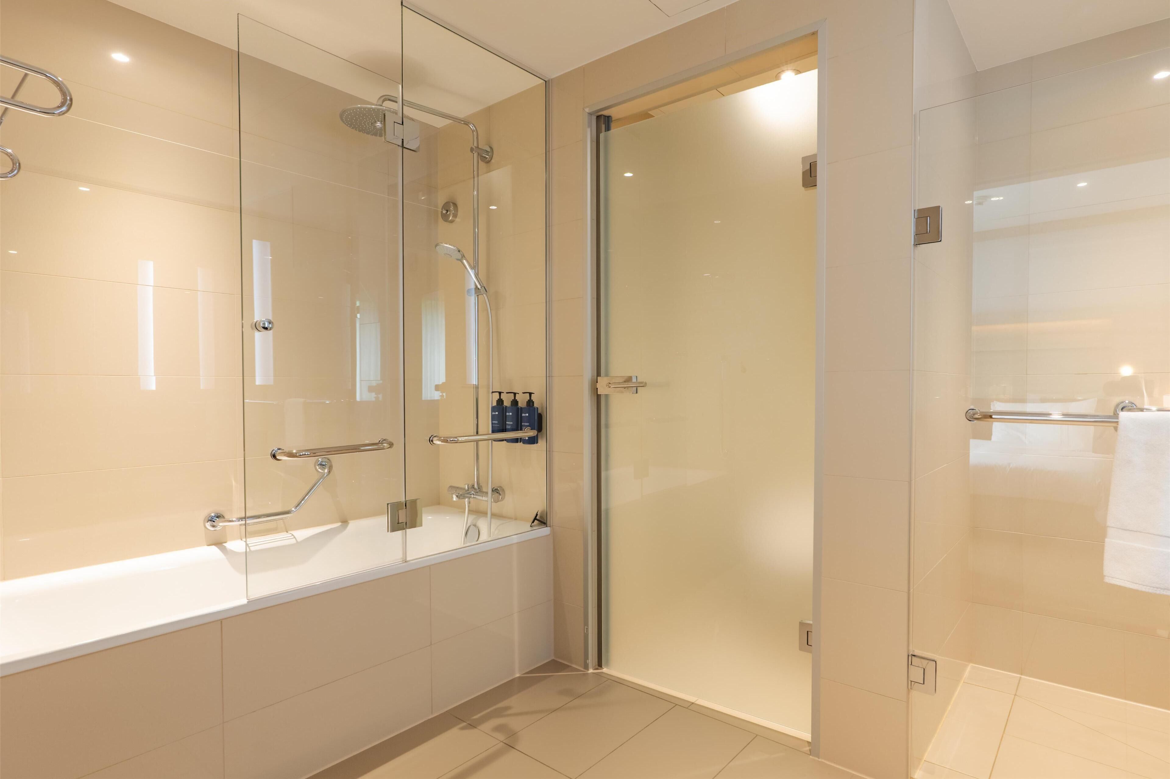 Ein modernes Badezimmer mit einer Glaskabine zur Dusche, einer freistehenden Badewanne und einer Glastür zu einem weiteren Raum.