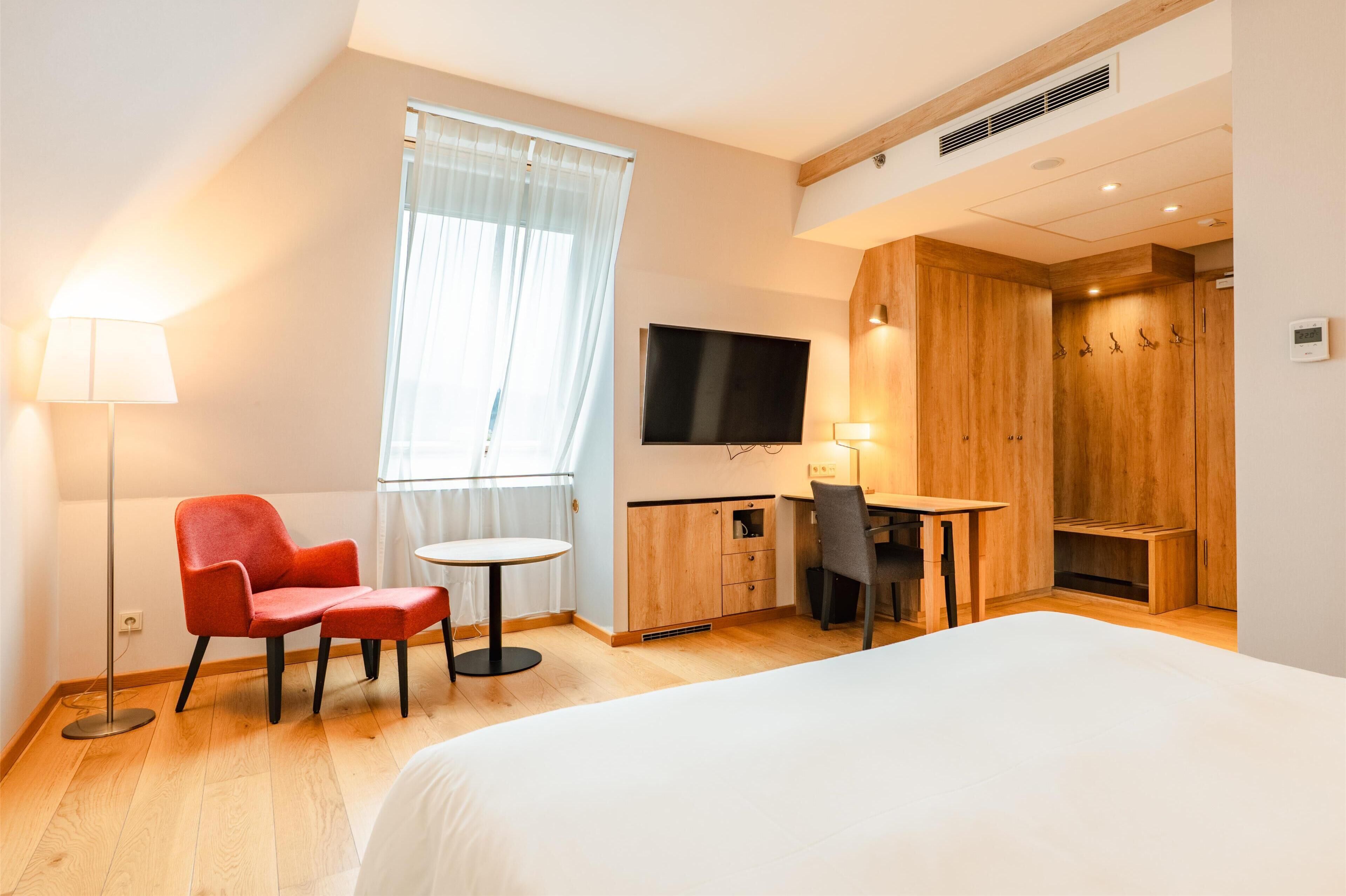 Una habitació d'hotel moderna amb un llit, un escriptori, una cadira, un televisor i un armari.
