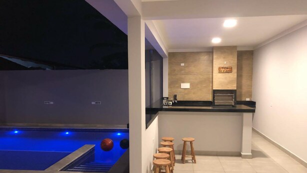 A modern indoor pool area with a bar and stools, a tiled floor, and a counter with a sign.