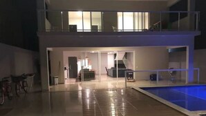 A modern two-story building with a swimming pool, a staircase, and a glass door leading to a living area.