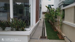 A narrow corridor with artificial grass, potted plants, and a glass wall reflecting a car and trees. - Palm Residence (George Town)