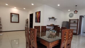 A dining area with a glass-top table, wooden chairs, a refrigerator, and a kitchen area with cabinets and a sink. - Palm Residence (George Town)