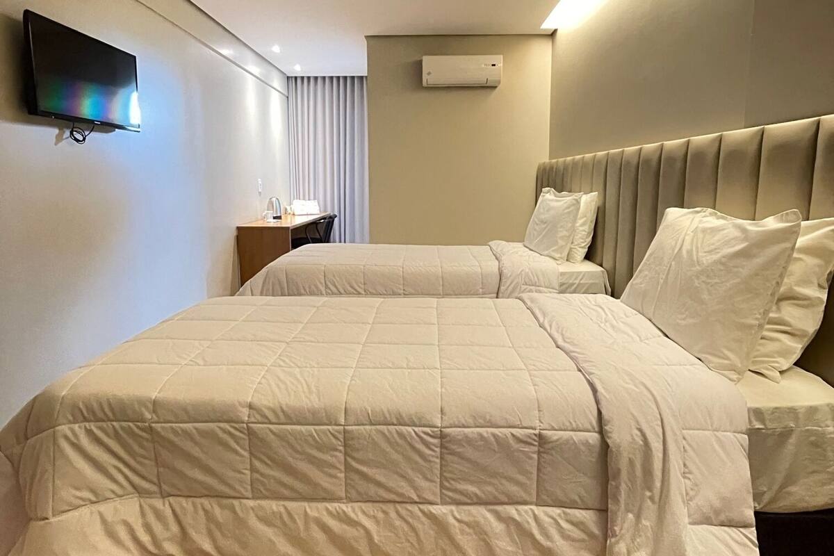 A hotel room with a large bed, a flat-screen TV mounted on the wall, an air conditioning unit, and a wooden floor.