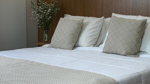 A neatly made bed with a patterned bedspread, a wooden headboard, and a vase with flowers on a bedside table. - Ouro Cerrado Palace Hotel (Patrocinio)