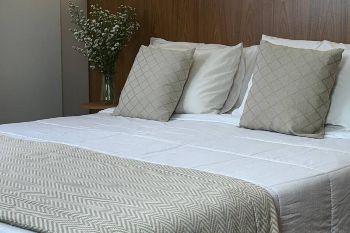 A neatly made bed with a patterned bedspread, a wooden headboard, and a vase with flowers on a bedside table.