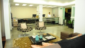 A reception area with two patterned chairs, a reception desk, and a receptionist. - Ouro Cerrado Palace Hotel (Patrocinio)