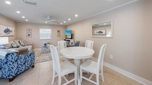 A dining area with a round table and white chairs, a sofa with a blue and white pattern, and a ceiling fan. - Sea Spray 2: *Pet-friendly *Steps to the beach *Close to shops, restaurants (Anna Maria)
