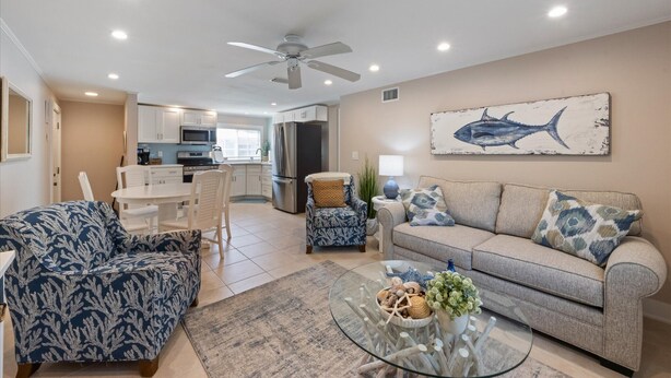A living room with a sofa, armchair, and coffee table, a kitchen in the background, and a ceiling fan. - Sea Spray 2: *Pet-friendly *Steps to the beach *Close to shops, restaurants (Anna Maria)