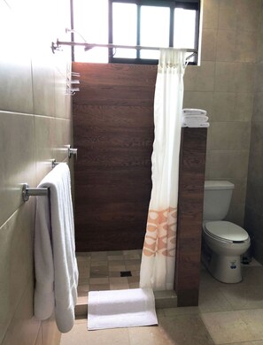 A bathroom with a wooden shower enclosure, a white toilet, and a towel rack with towels.