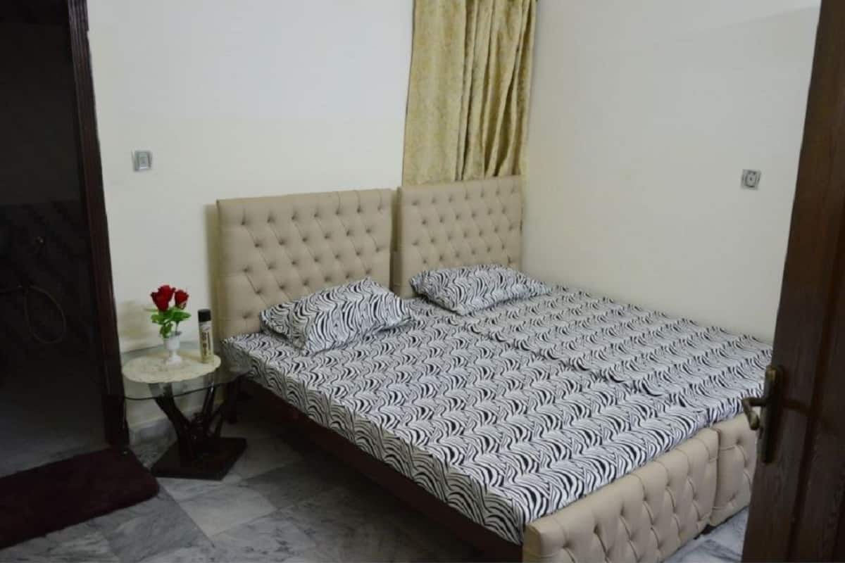 A bedroom with a tufted headboard, a zebra-patterned bedspread, a small round table with a vase of red roses, and a curtain on the window.