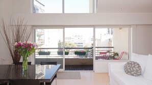 A modern living room with a glass door leading to a balcony, a dining area with a table and chairs, and a white sofa with a patterned pillow. - Billinghurst 2 by Be Local Argentina (Buenos Aires)