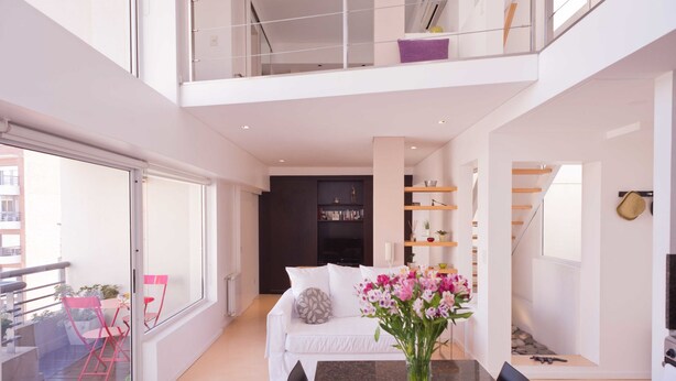 A modern, open-plan living space with a dining area, a sofa, and a glass door leading to a balcony. - Billinghurst 2 by Be Local Argentina (Buenos Aires)