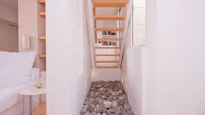 A narrow hallway with a wooden staircase, a small white table with a glass of water, and a white sofa. - Billinghurst 2 by Be Local Argentina (Buenos Aires)