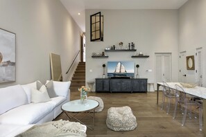 Ein modernes Wohnzimmer mit einem weißen Sofa, einem runden Couchtisch und einem Essbereich mit einem Glastisch und Stühlen.