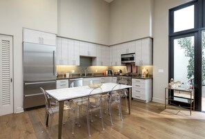 A modern kitchen with stainless steel appliances, a marble countertop, and a dining area with transparent chairs.