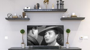 A modern living room with a large flat-screen TV, dark wood cabinetry, and decorative shelves above. - Luxury Condo in Heart of Downtown Santa Barbara  (Santa Barbara)