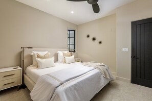 A bedroom with a bed, nightstands, a ceiling fan, a window, and a door.
