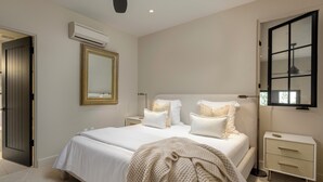 A bedroom with a bed, bedside tables, a mirror, an air conditioning unit, and a window.