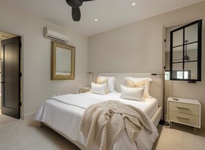 Une chambre à coucher comprenant un lit, des tables de chevet, un miroir, un appareil de climatisation et une fenêtre.
