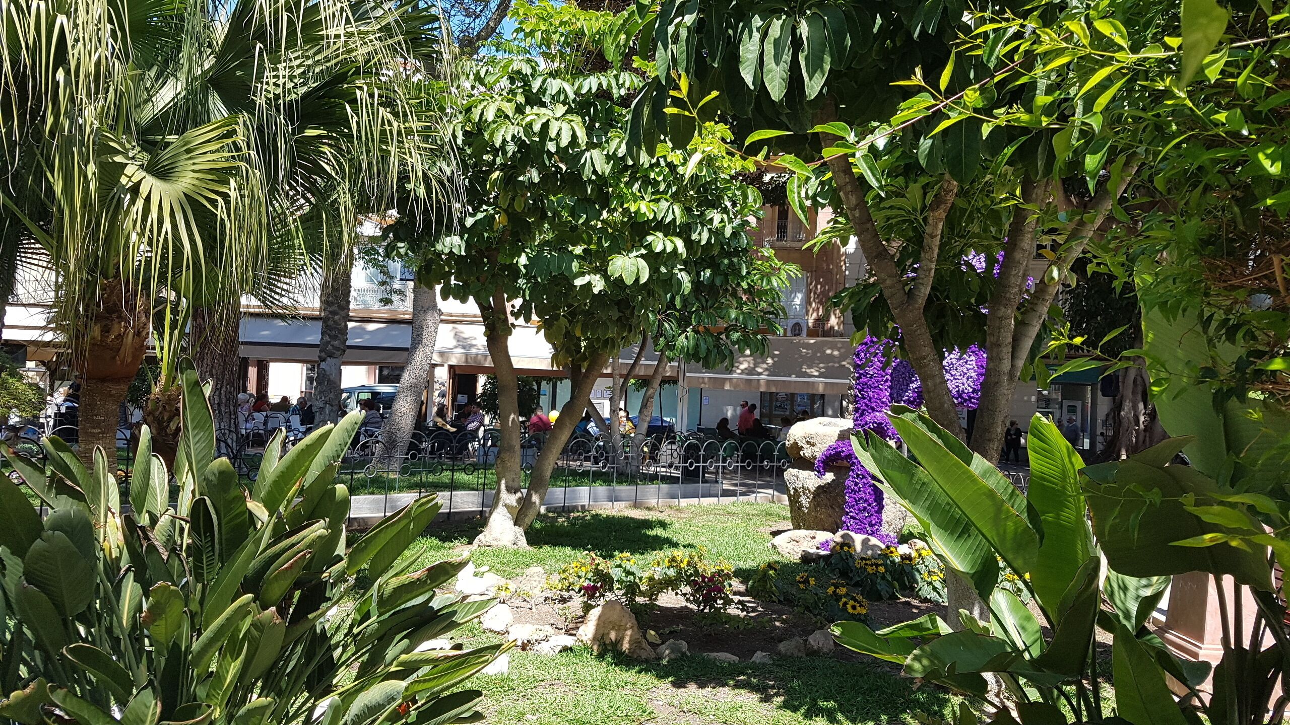 Une cour intérieure agrémentée de palmiers, d’une fontaine et de fleurs violettes.
