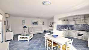 Um espaço de estar compacto com área de jantar, um sofá listrado, uma cozinha pequena com azulejos azuis e um lustre.