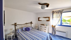 Um quarto com cama, cômoda, mesa de cabeceira, espelho e janela com cortinas.