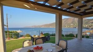 An outdoor patio with a table set for dining, overlooking a coastal view with mountains in the distance. - Brand New Villa with Private Pool and Panoramic Mountains and Sea Views (Paphos)