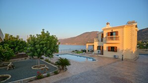 A pool area with a view of the sea and mountains, surrounded by a building with a balcony. - Brand New Villa with Private Pool and Panoramic Mountains and Sea Views (Paphos)