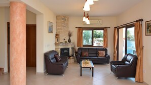 A living room with a fireplace, leather sofas, a coffee table, and large windows with curtains. - Brand New Villa with Private Pool and Panoramic Mountains and Sea Views (Paphos)