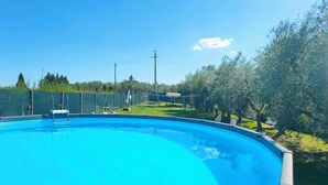 Piscina blu cristallina circondata da un'area recintata con alberi e un prato verde.