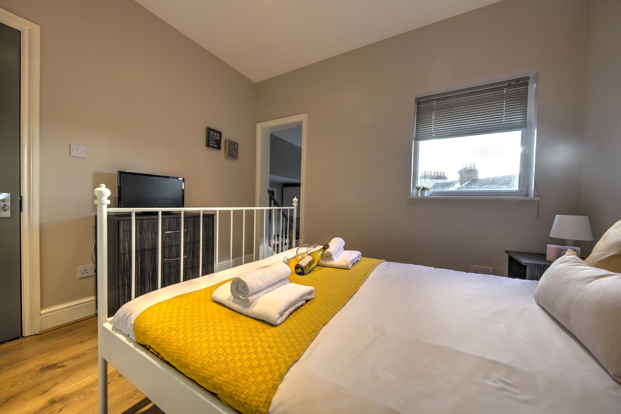 A hotel room with a bed, a television, a window with blinds, and a view of buildings outside.